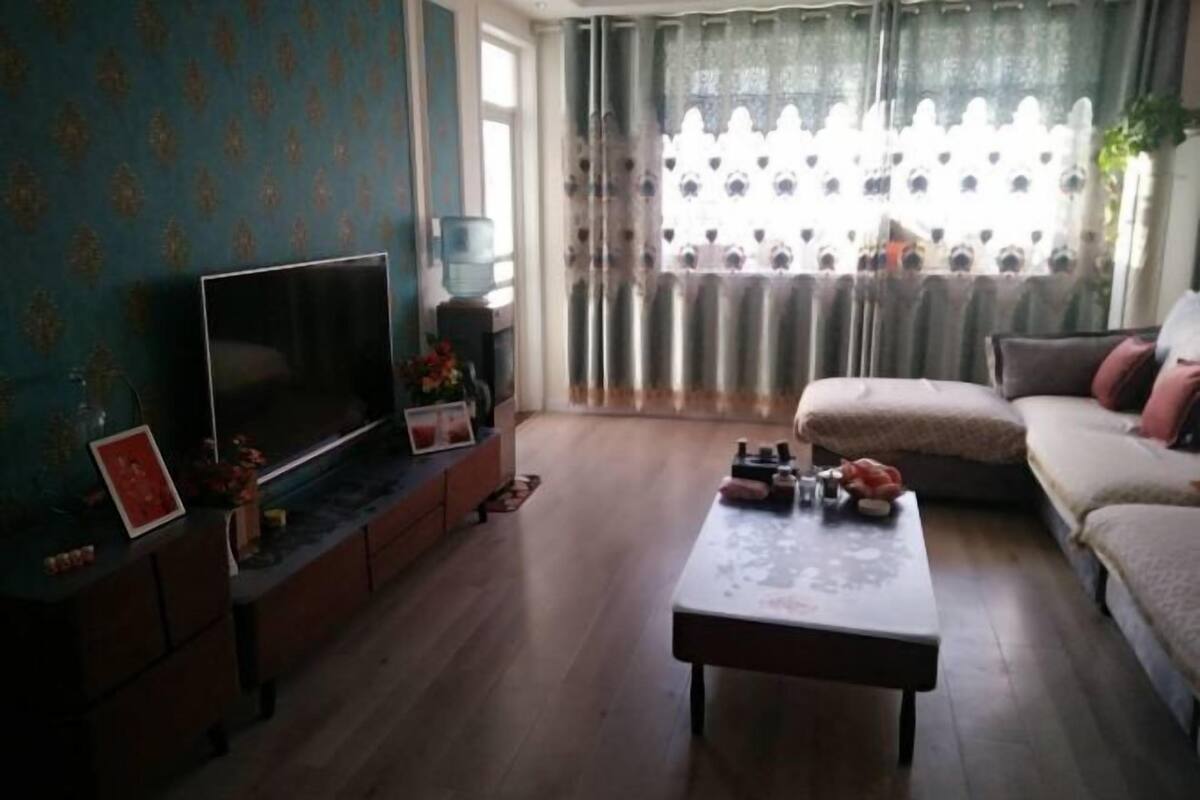 A living room with a flat-screen TV, a sofa, a coffee table, and a window with curtains.