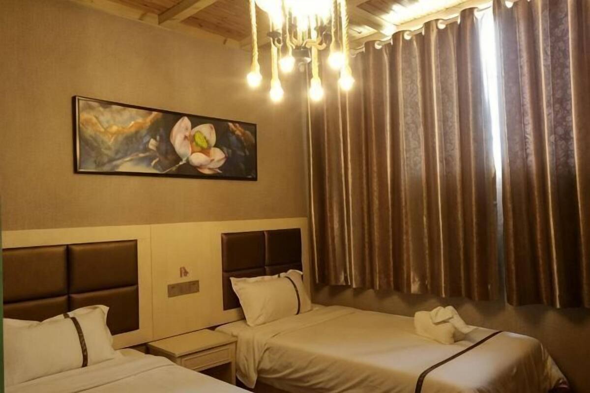 A hotel room with two beds, a painting, a chandelier, and curtains.