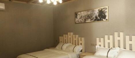 A room with two beds, a ceiling light fixture, and a wall-mounted artwork.