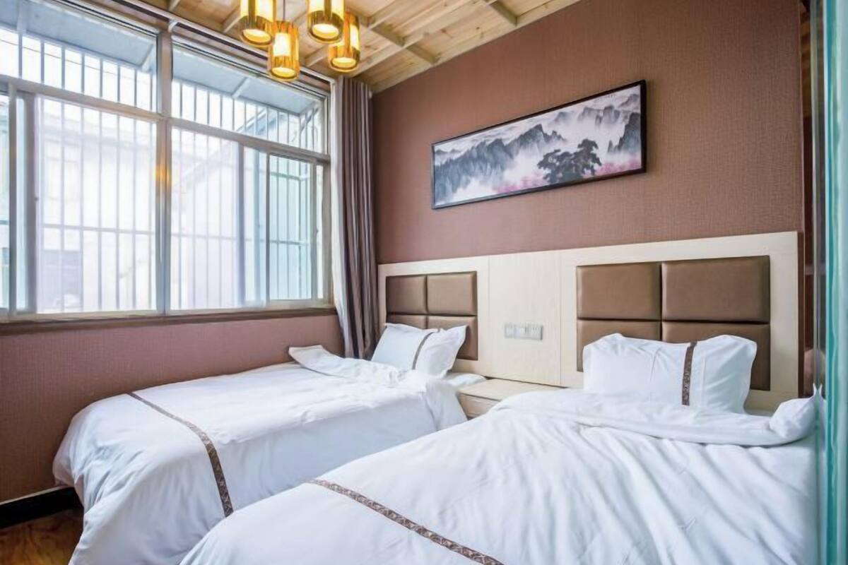 A hotel room with two beds, a large window, and a painting on the wall.