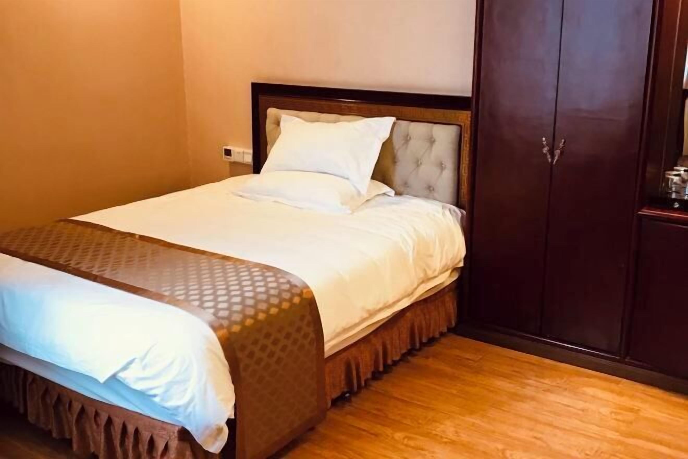 A neatly made bed with a wooden headboard, a wooden wardrobe, and a wooden floor.