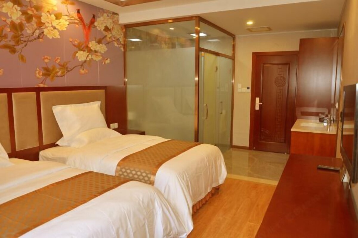 A hotel room with two beds, a glass partition, a wooden door, and a small bathroom area.