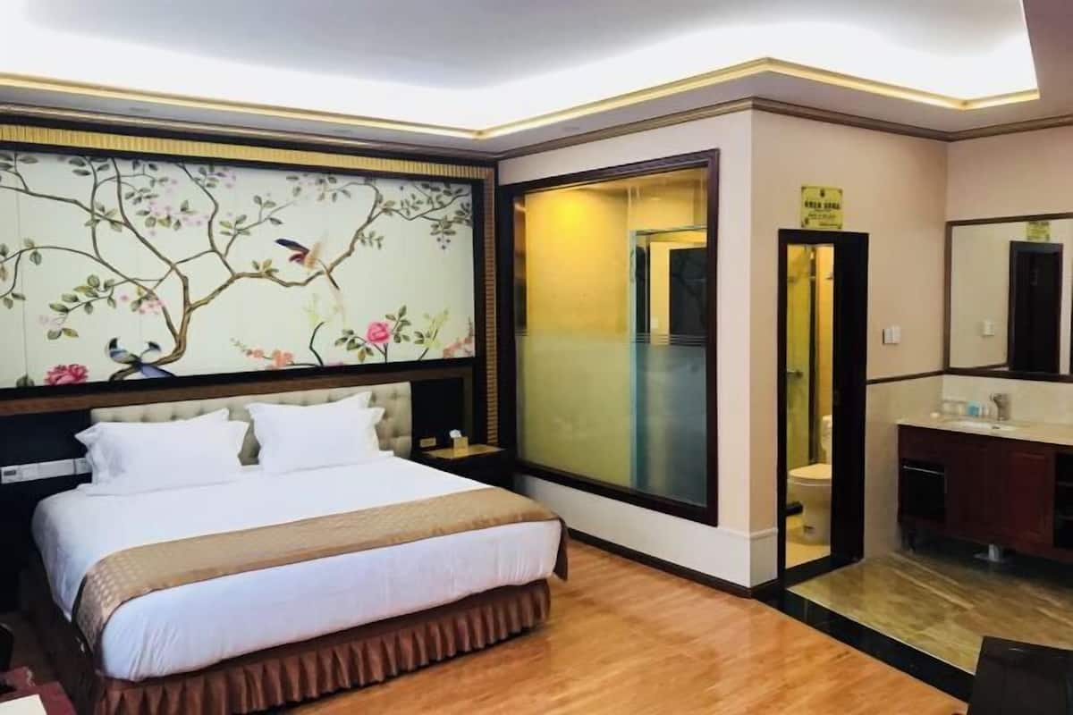 Habitación de hotel con cama, mesita de noche, espejo y baño visible a través de una puerta de cristal.