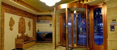 A hotel lobby with a marble floor, a chandelier, a revolving door, and a wall-mounted display.