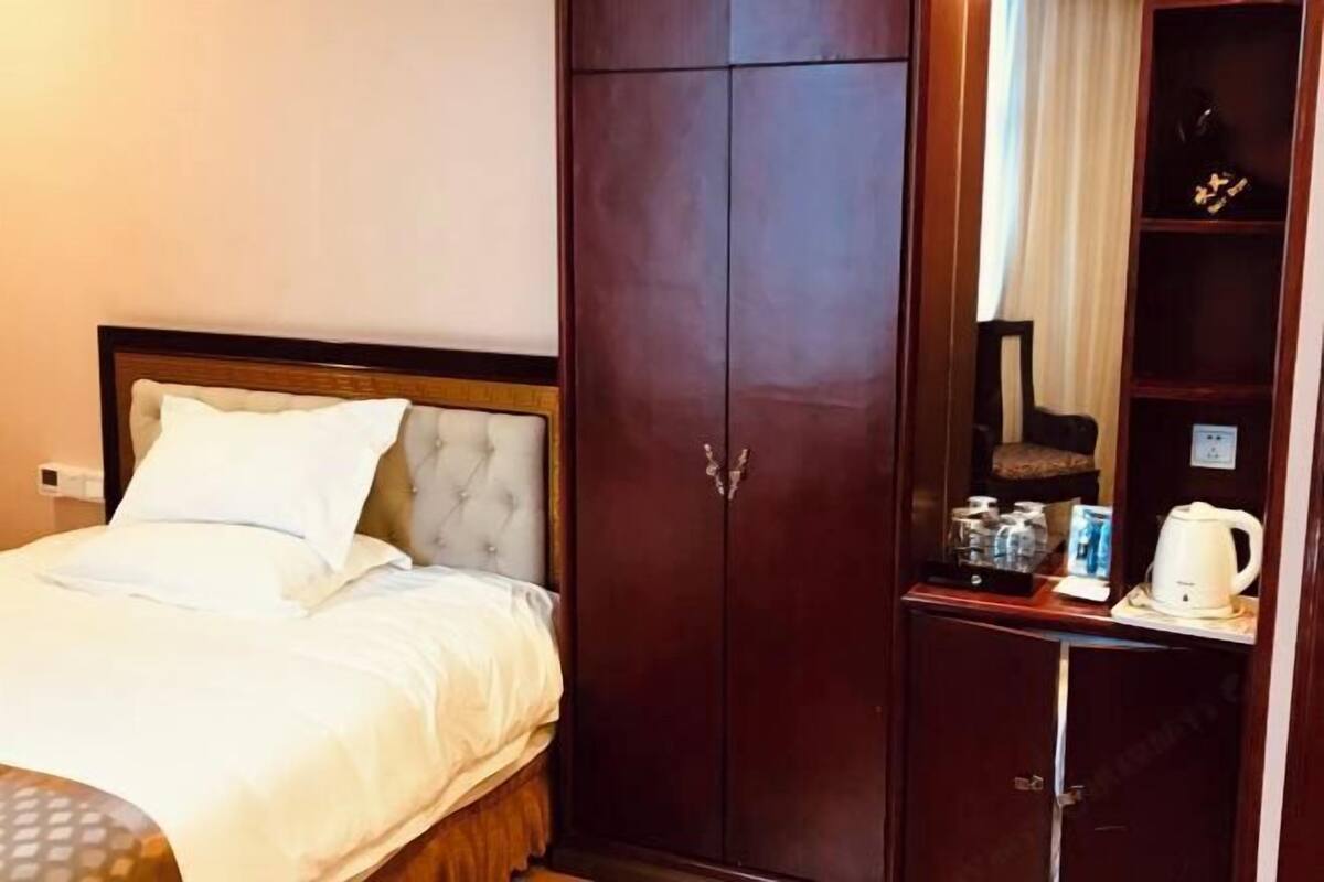 Habitación de hotel con cama, armario y una mesita con hervidor y tazas.