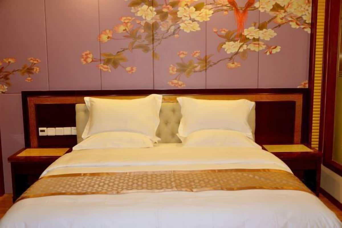Habitación de hotel con una cama grande, dos mesitas de noche y una pared decorada con un mural floral.