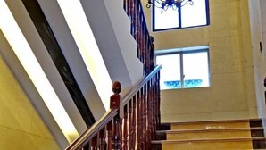 A staircase with wooden balusters and a metal handrail, leading to a landing with a large window and a chandelier.