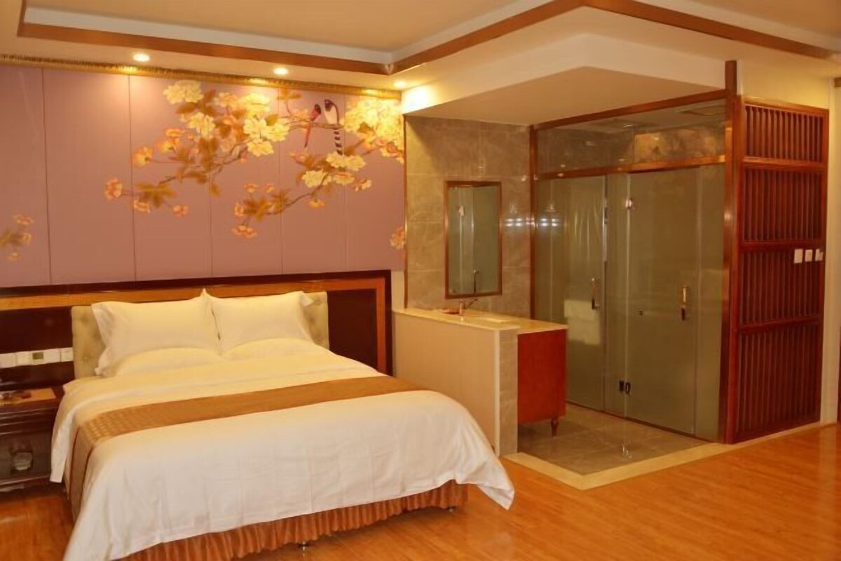 A hotel room with a large bed, a vanity with a mirror, and a walk-in shower.