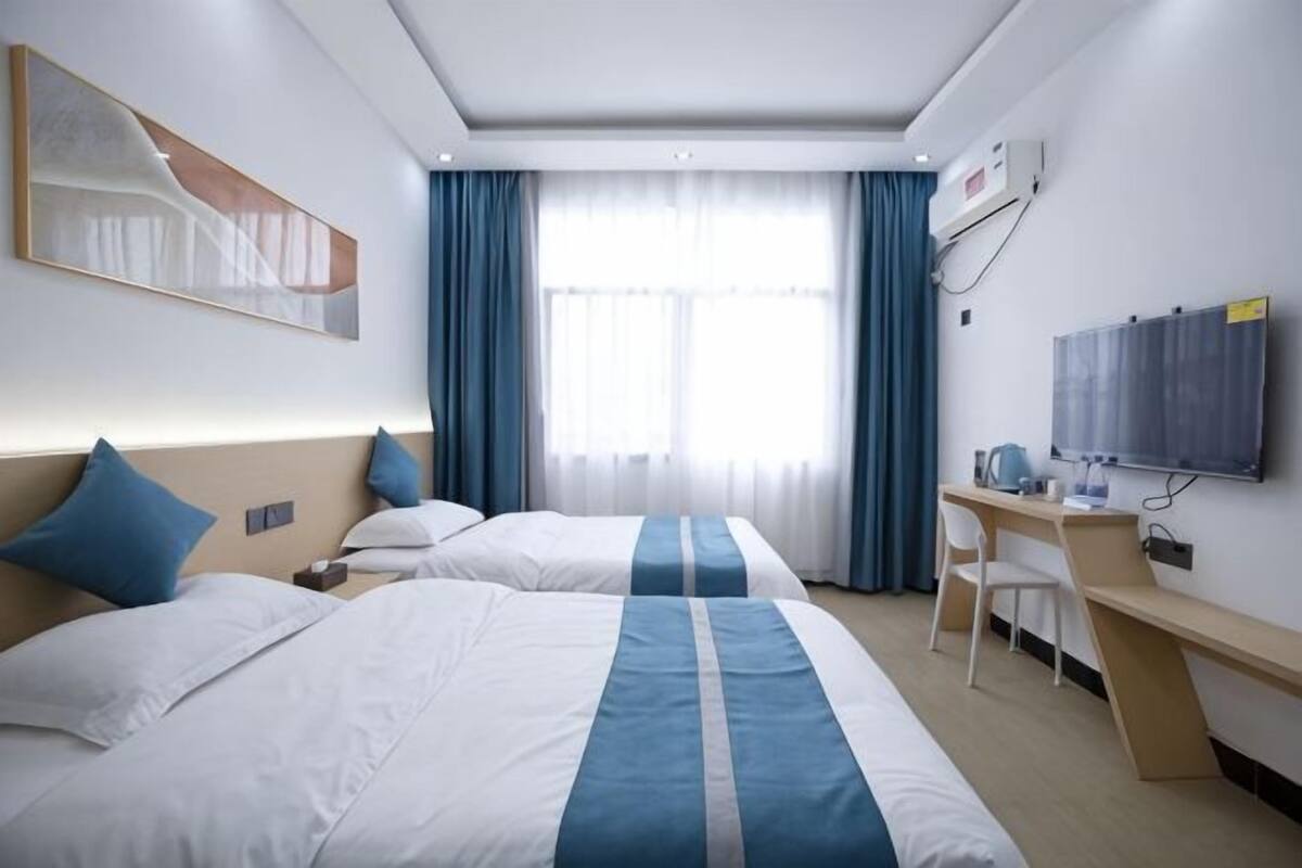A hotel room with two beds, a desk, a chair, a TV, and a window with curtains.