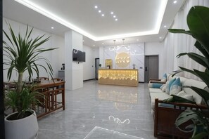 Un moderno vestíbulo de hotel con recepción, zona de estar y una planta grande en maceta.