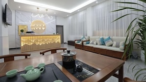 Una sala de estar moderna con un sofá, una mesa de comedor con teteras, una zona de cocina con mostrador y un televisor montado en la pared.