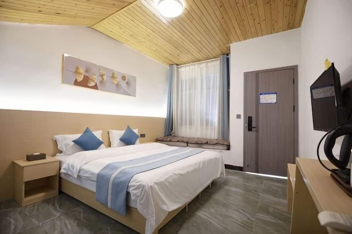A hotel room with a bed, bedside table, a desk with a chair, a television, and a window with curtains.