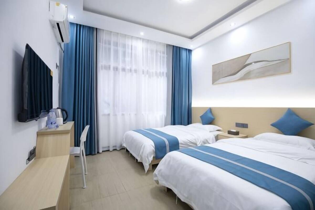 A hotel room with two beds, a desk, a chair, a TV, and a window with curtains.