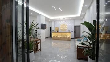 Un vestíbulo de hotel con mostrador de recepción, zona de estar y plantas en macetas.