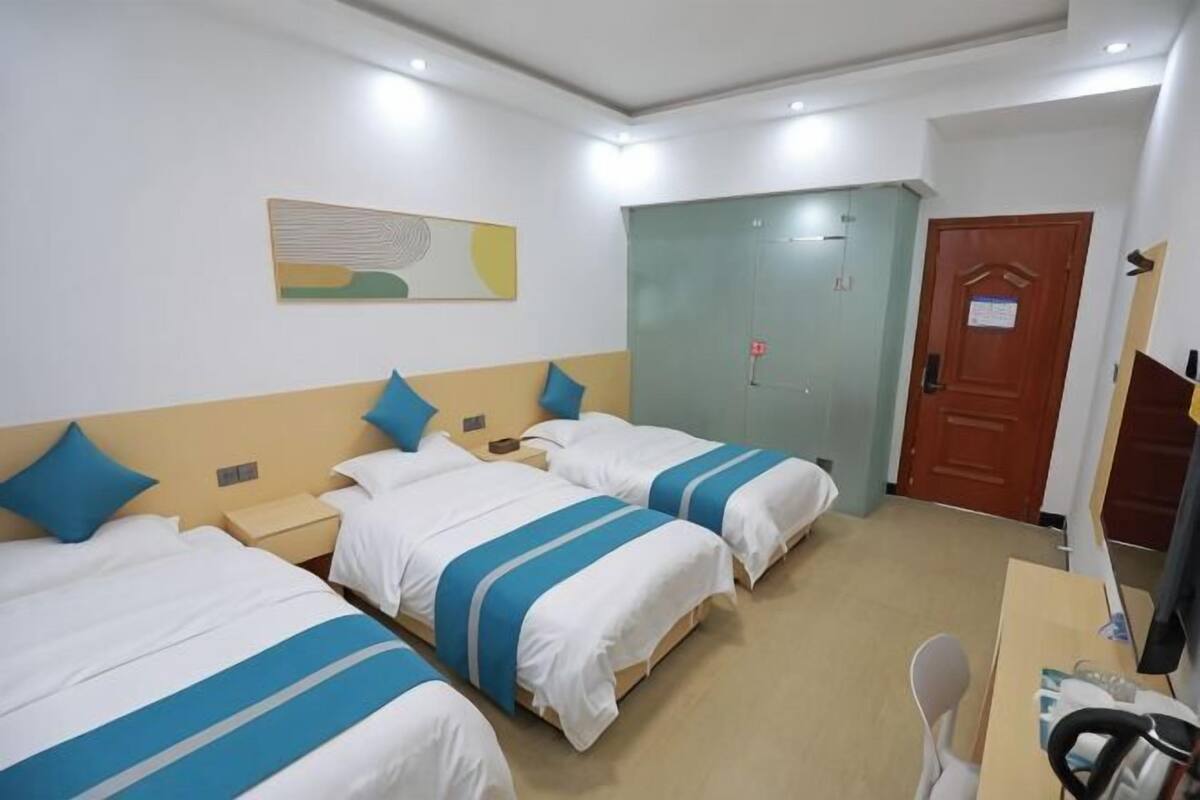 A hotel room with three beds, a desk, a chair, a wardrobe, and a door.