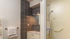 Ett badrum med en duschkabin i glas, en vit handfat med en spegel ovanför och en handdukshängare med en vit handduk.