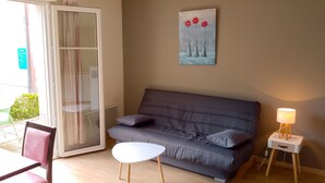 Ett vardagsrum med en grå soffa, ett litet vitt bord, en lampa och en tavla på väggen.