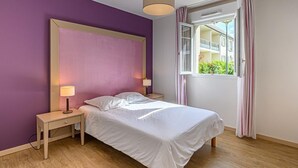 Un dormitorio con cama, mesitas de noche, una lámpara, una ventana con cortinas y vistas a edificios.