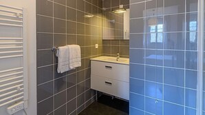 Un baño moderno con baldosas grises oscuras, una toalla blanca en un perchero, un lavabo con espejo y un calentador empotrado.