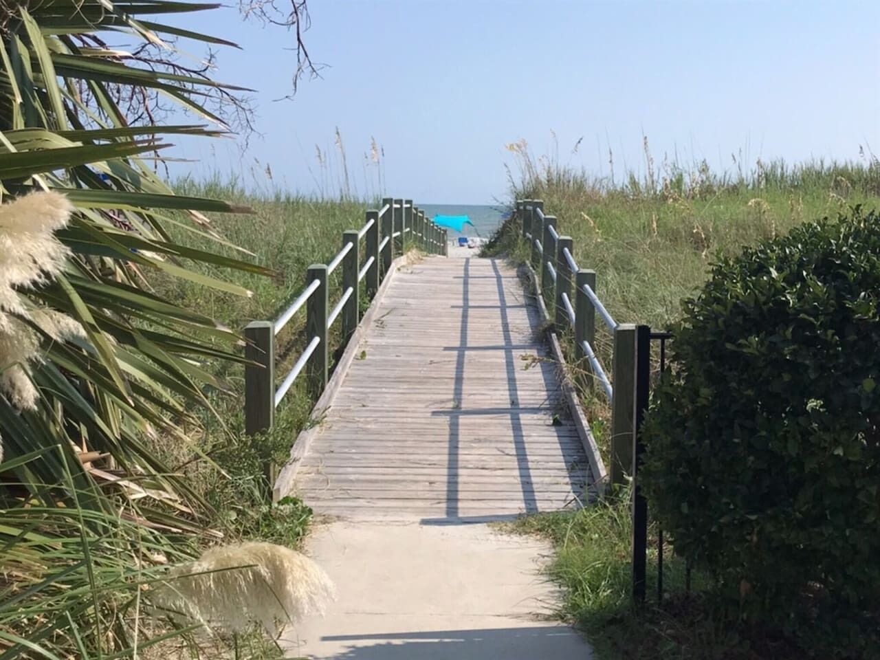 A wooden boardwalk leading to a beach with a clear sky.