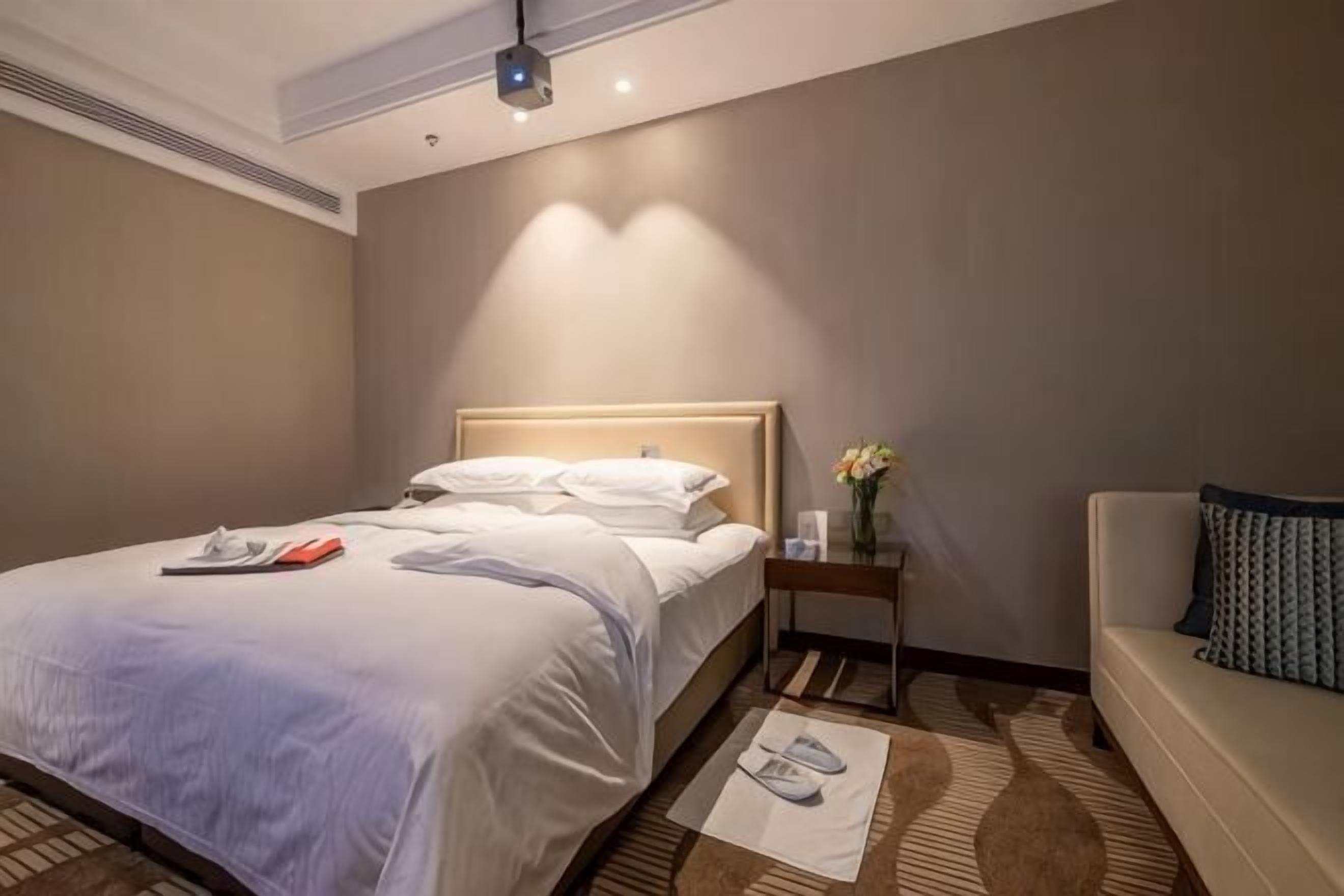 A hotel room with a bed, bedside table, nightstand, and a couch.