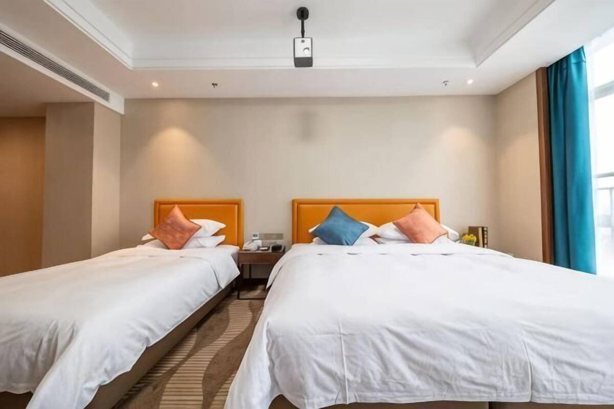 Une chambre d’hôtel avec deux lits, un panneau de commande fixé au plafond, une table de chevet et une fenêtre avec des rideaux.