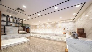 Een moderne hotellobby met een marmeren receptiebalie, houten vloeren en een glazen vitrinekast met boeken.