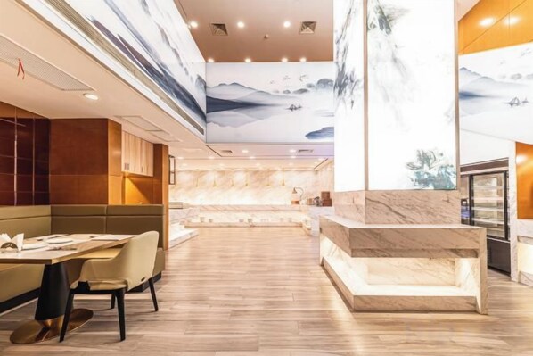 Un vestíbulo de hotel moderno con una zona de estar central, un mostrador de recepción de mármol y un mural grande en el techo.