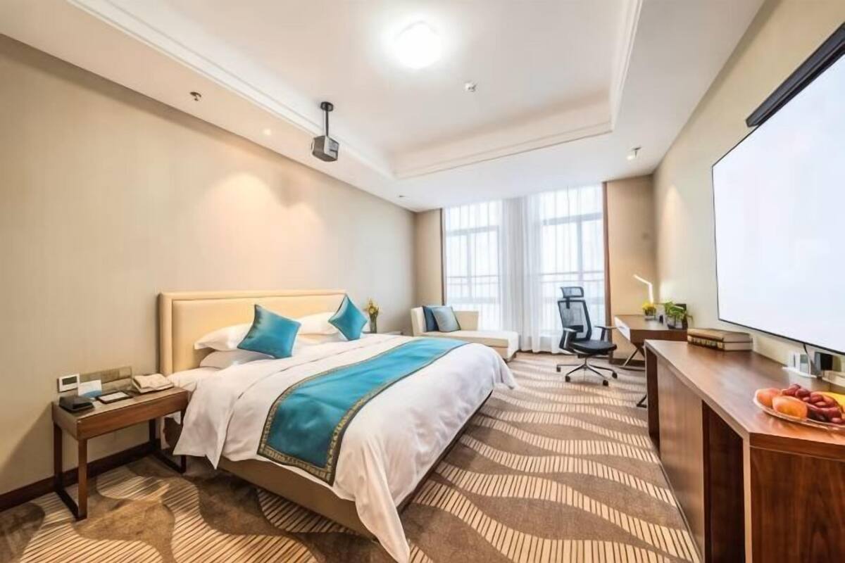 Une chambre d’hôtel avec un lit, un bureau, une chaise et une grande fenêtre.