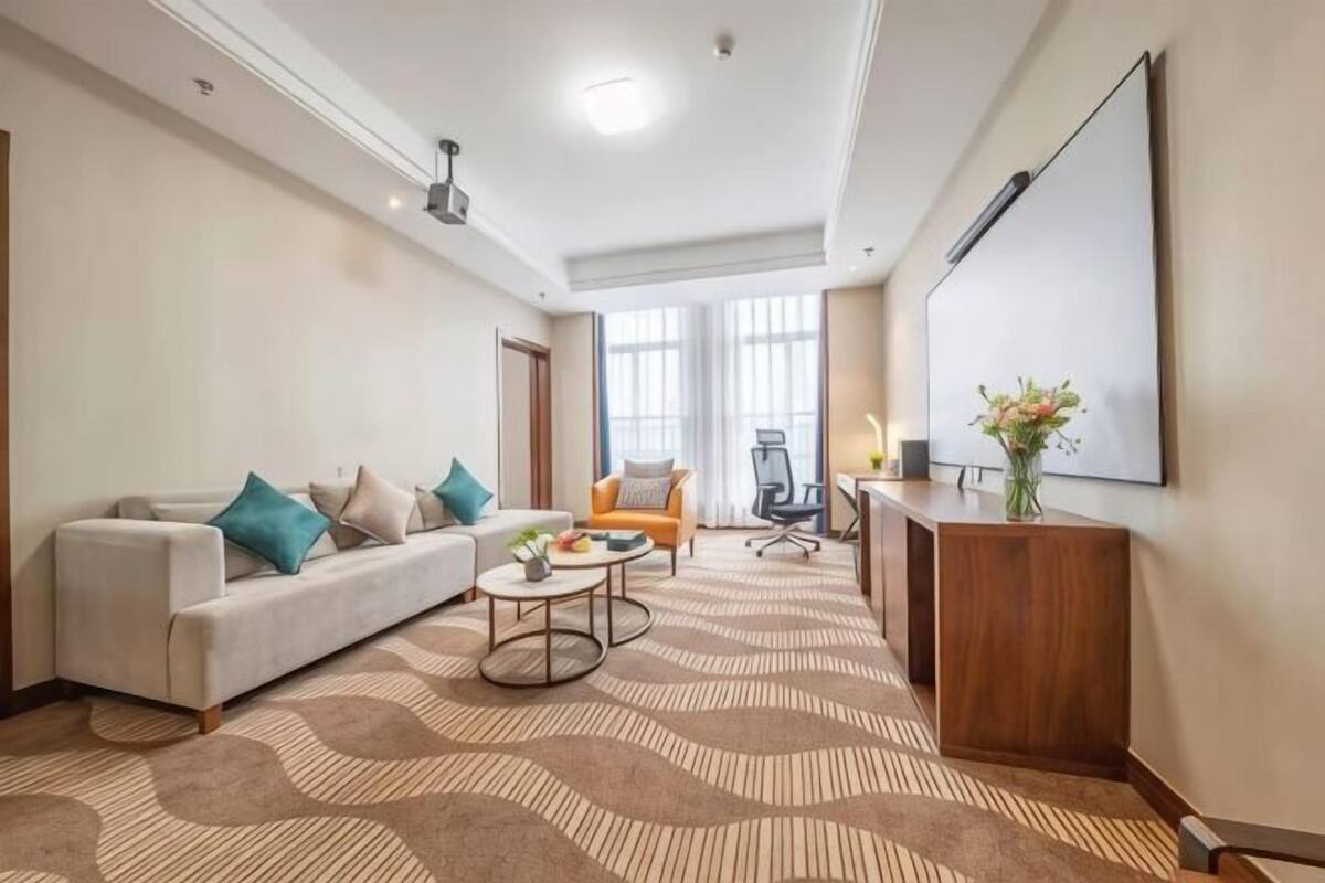Une chambre d’hôtel moderne équipée d’un canapé, d’un fauteuil, d’une table basse, d’un bureau et de grandes fenêtres.