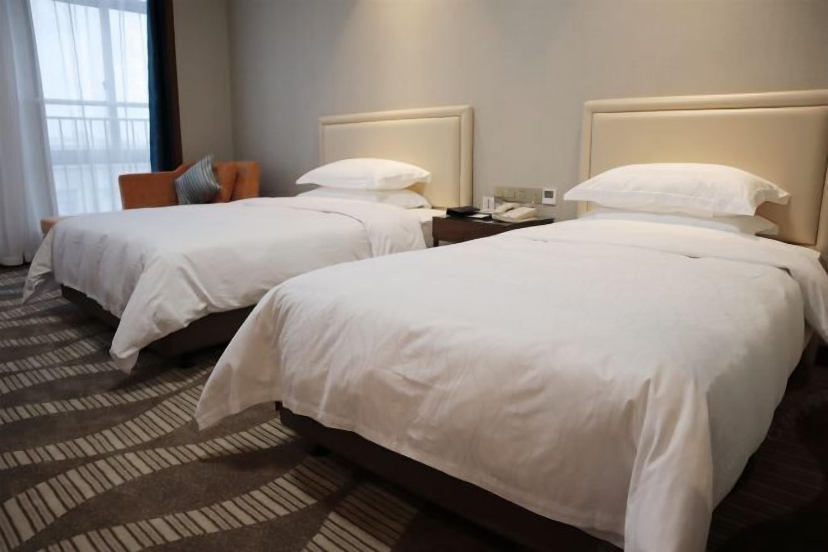 Two double beds with white linens, a nightstand with a phone, and a patterned carpet.