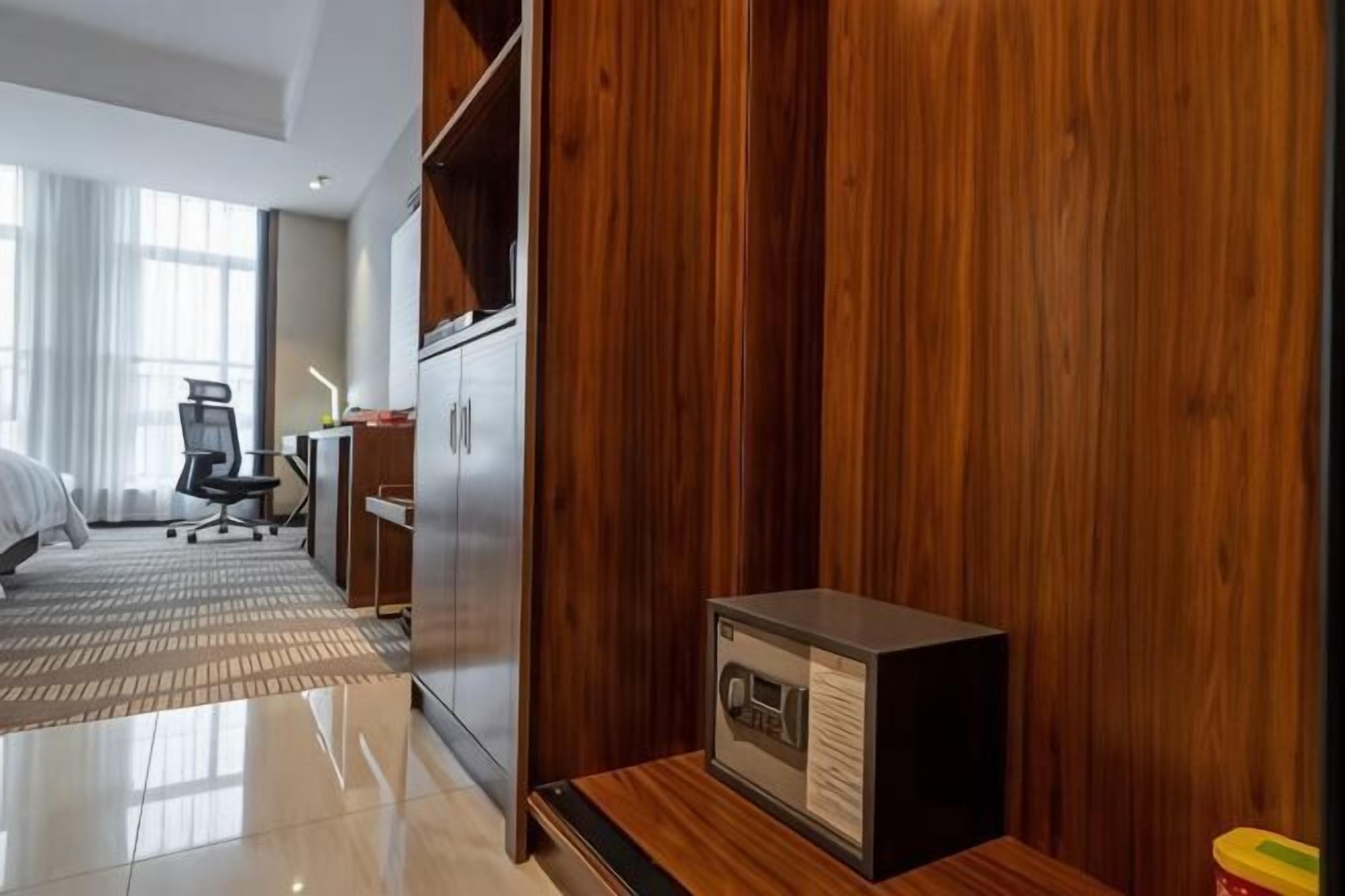 A hotel room with a wooden wardrobe, a desk with a chair, a bed, and a small safe.