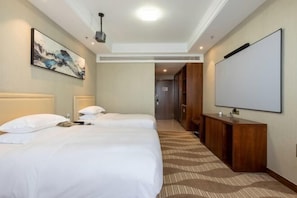 A hotel room with two beds, a large wall-mounted TV, a wooden console, and a hallway leading to a door.