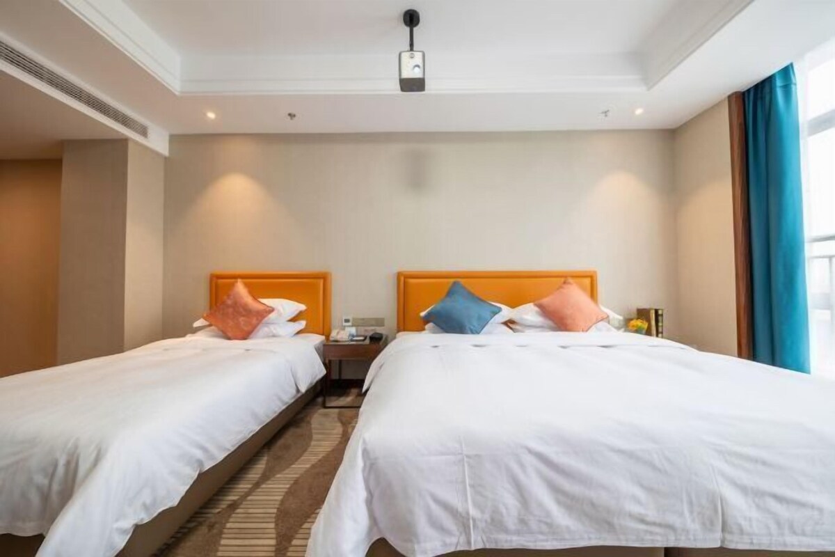 A hotel room with two beds, a nightstand, a lamp, and a window with curtains.