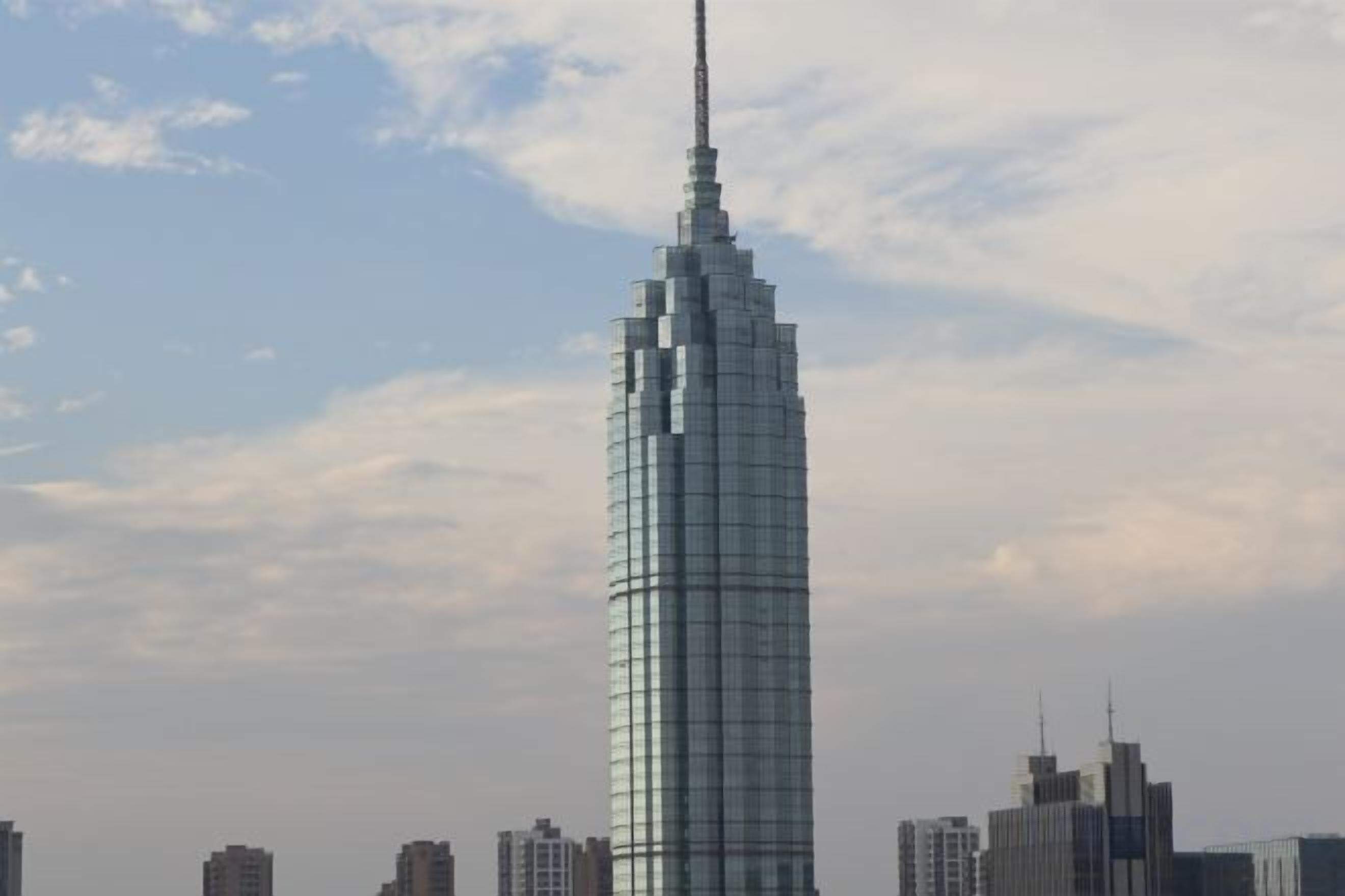 Un rascacielos alto y moderno con un pináculo distintivo, rodeado de otros edificios.