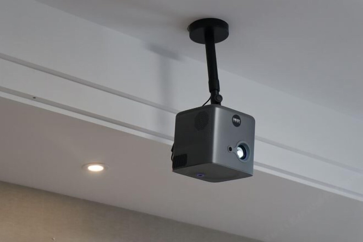 A ceiling-mounted projector with a black cord, a power button, and a lens.
