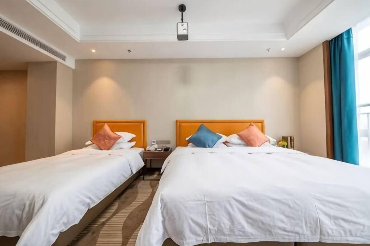 Une chambre d’hôtel avec deux lits, une table de chevet, une horloge et une fenêtre avec des rideaux.
