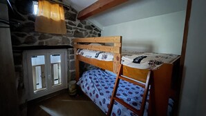 Ein Stockbett in einem rustikalen Zimmer mit Steinwänden und Holzbalkendecke.