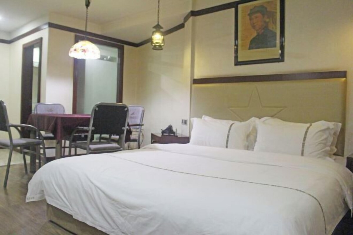 A hotel room with a large bed, a desk with a chair, and a hanging lamp.
