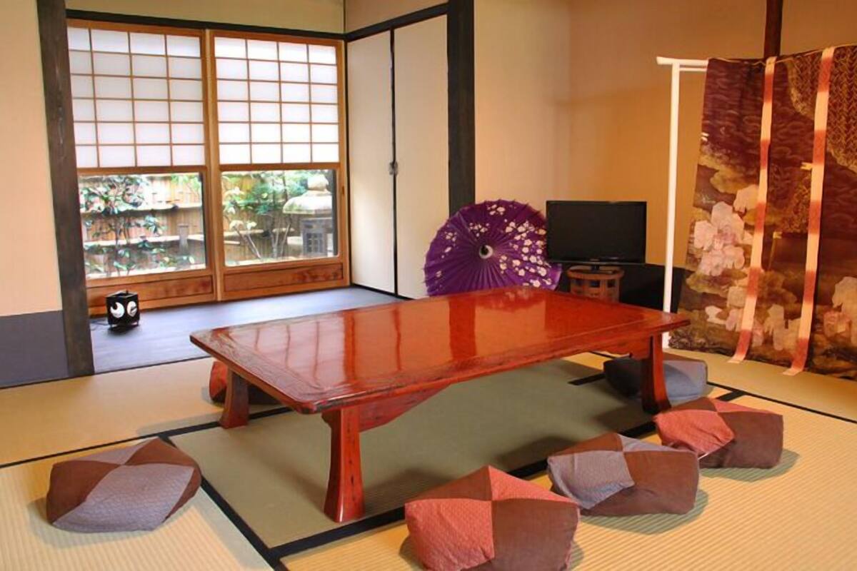 A traditional Japanese room with tatami flooring, a low wooden table, and a sliding door with a view of greenery outside.