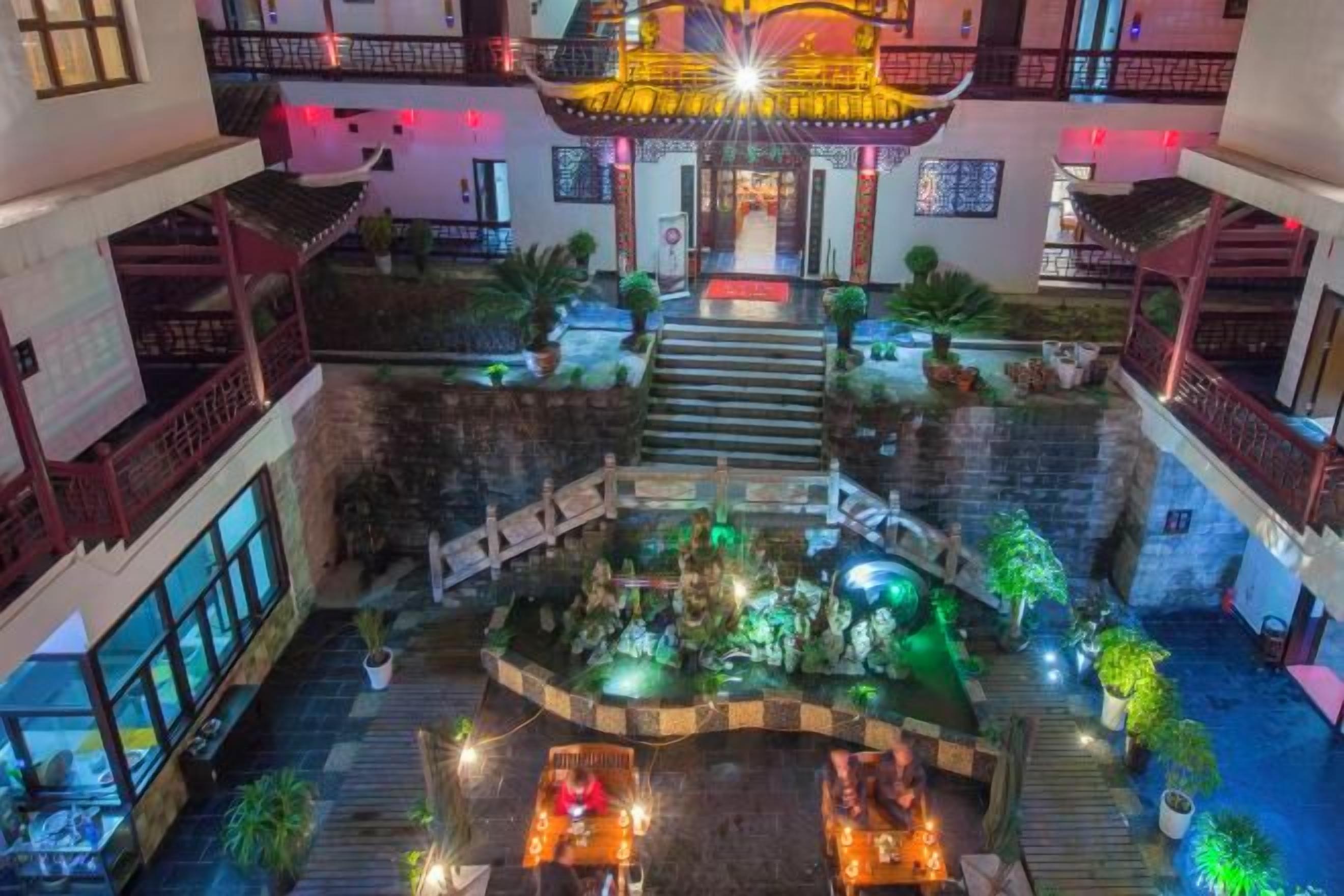 Un atrio de hotel de varios niveles con una escalera central, plantas de interior y una fuente decorativa.