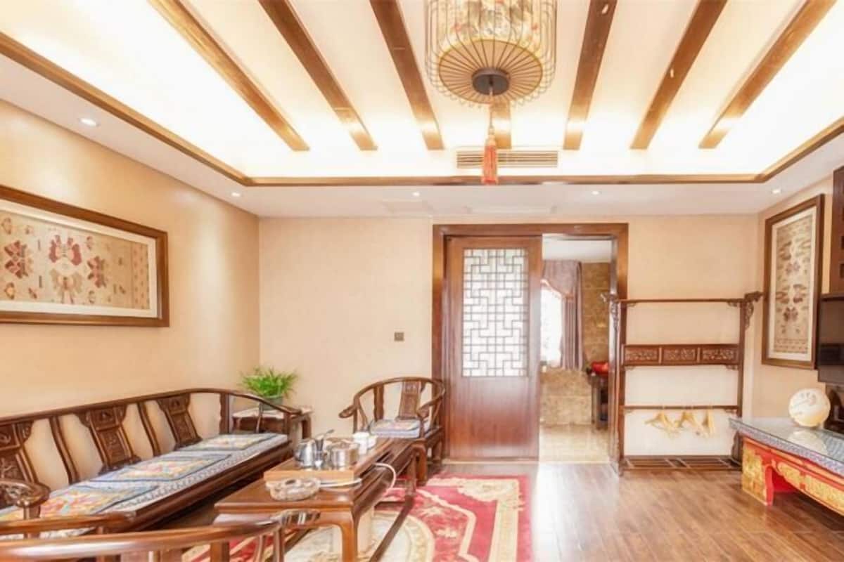 A traditional-style room with a long wooden dining table, chairs, a patterned sofa, and a decorative ceiling light fixture.