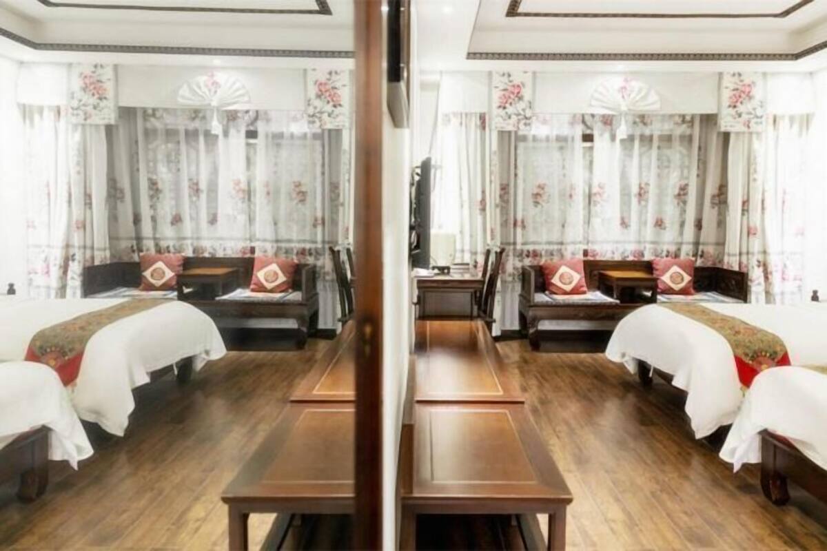 A mirrored hotel room with two beds, wooden flooring, floral curtains, and a central table.