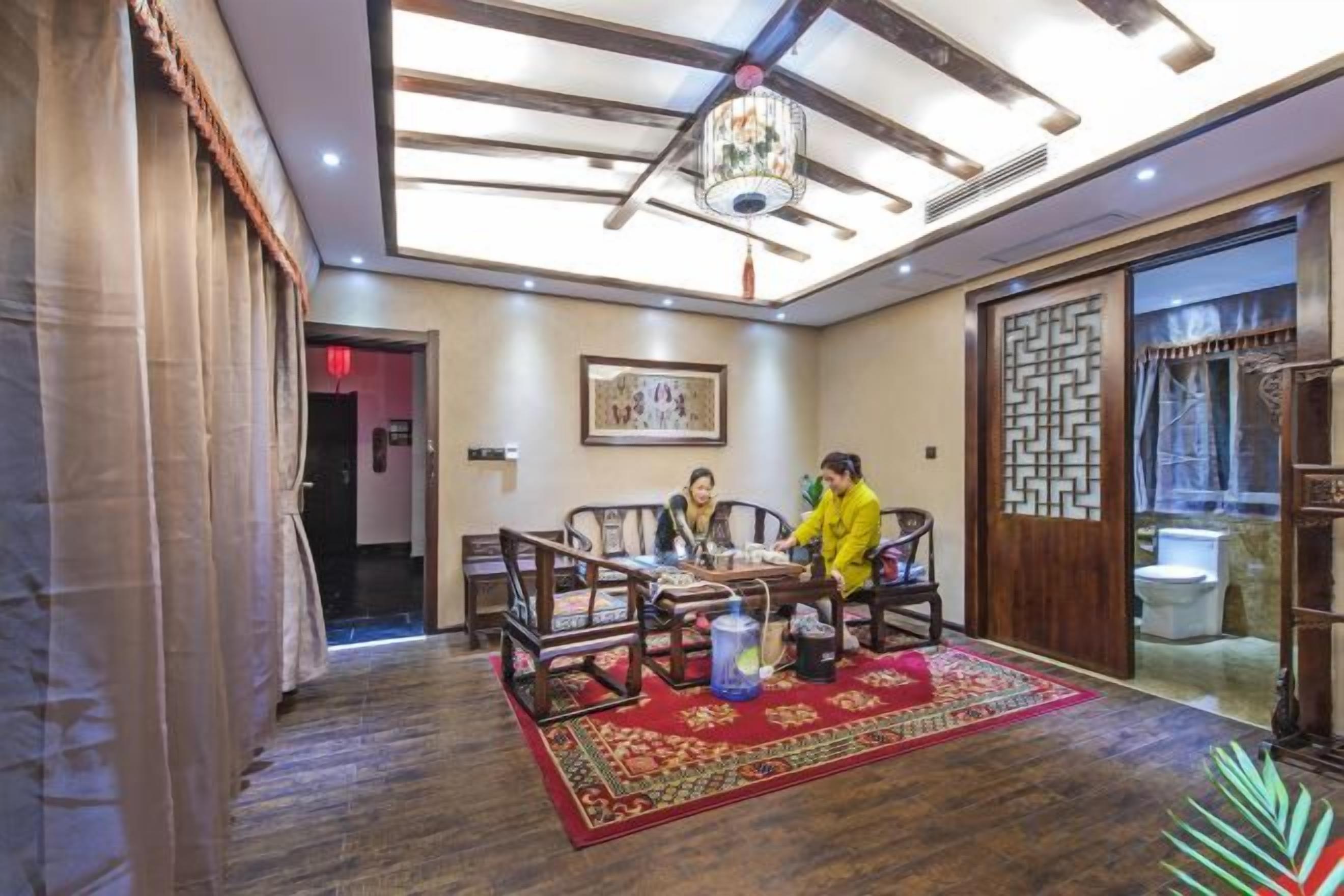 Una habitación tradicional con piso de madera, un tapete rojo con estampado, una araña y una puerta de madera con diseño geométrico.