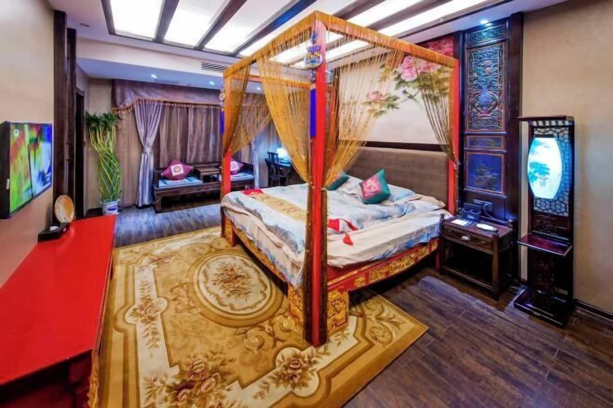 A four-poster bed with a canopy, a red desk, a large ornate rug, and a traditional decorative screen.