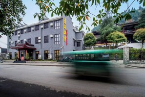 Un edificio de estilo arquitectónico tradicional, un autobús verde en movimiento y un cielo despejado.