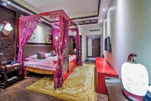 Una cama tradicional con dosel rojo, una mesita de noche de madera, un banco rojo y una lámpara de pared.