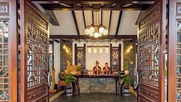 A reception area with a reception desk, two receptionists, a chandelier, and traditional wooden decor.
