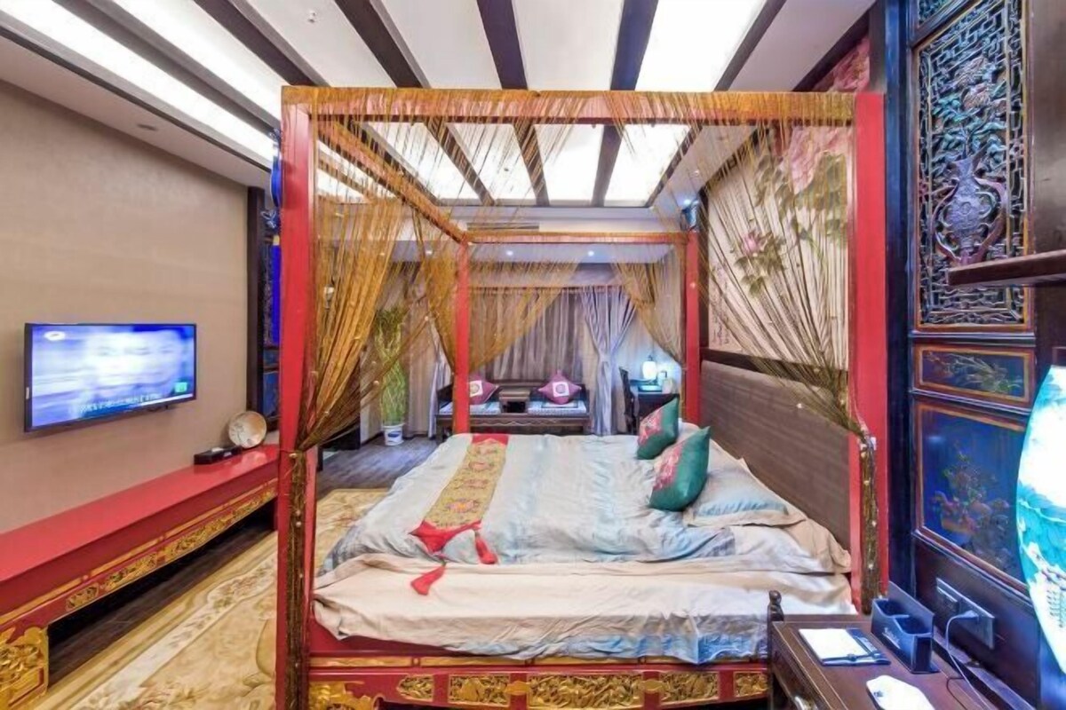 Un lit à baldaquin, un téléviseur fixé au mur et un paravent décoratif sur le côté droit.