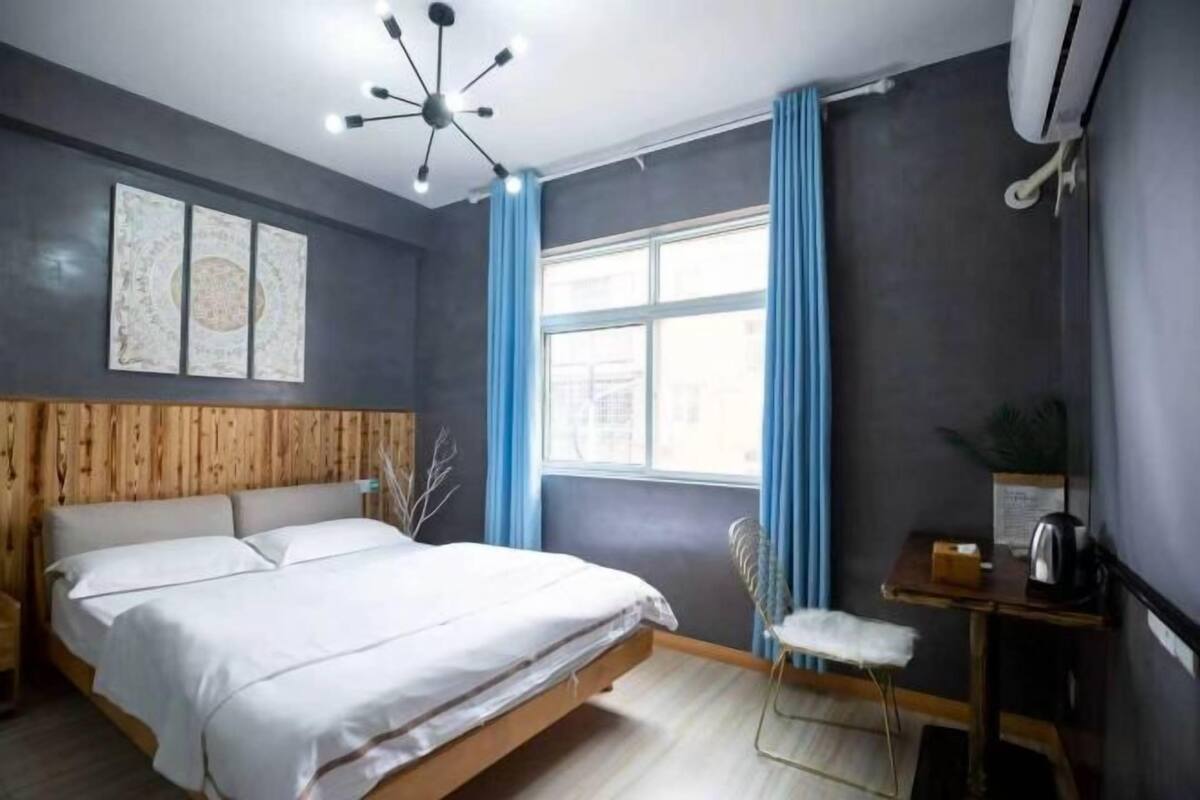 Un dormitorio moderno con una cama, una mesita pequeña, una silla, una ventana con cortinas y una lámpara en el techo.